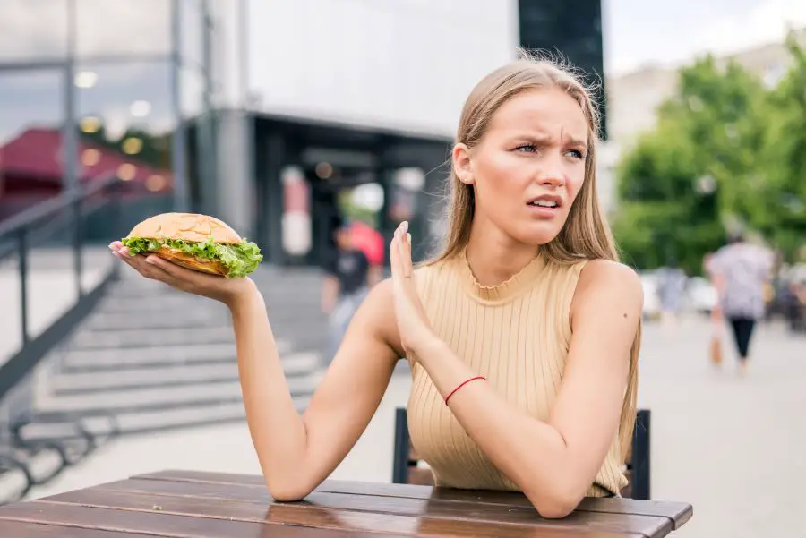 young sad woman holding burger satisfied while sitting outdoors fast food